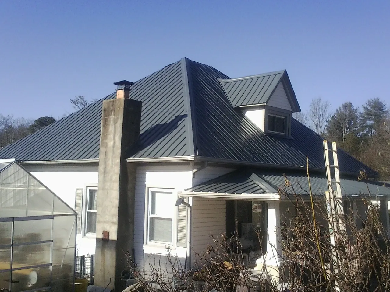 Dark blue standing seam metal roof on a white farmhouse with dormer — Slate & Tile Roof Repair by Roofing Brothers in Springville