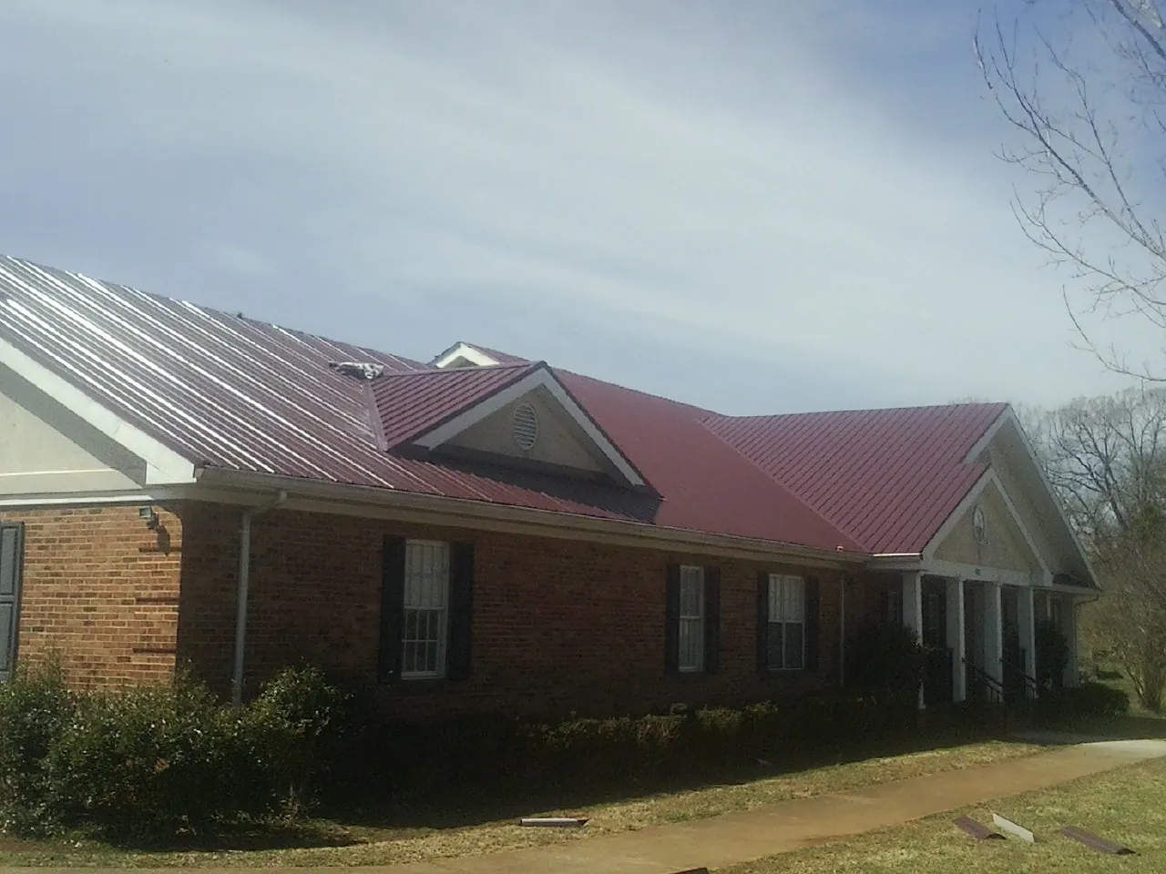 Red metal roof with gabled entries on a long brick building, from a Hail Damage Roof Repair job in Springville